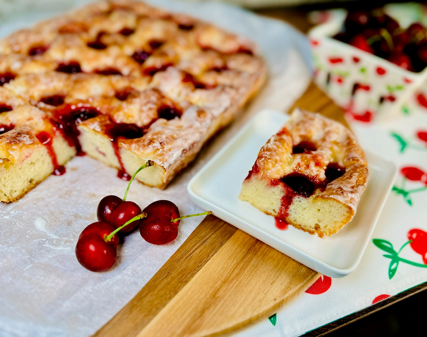 Slice of Cherries Jubilee Focaccia on a white plate with fresh cherries nearby