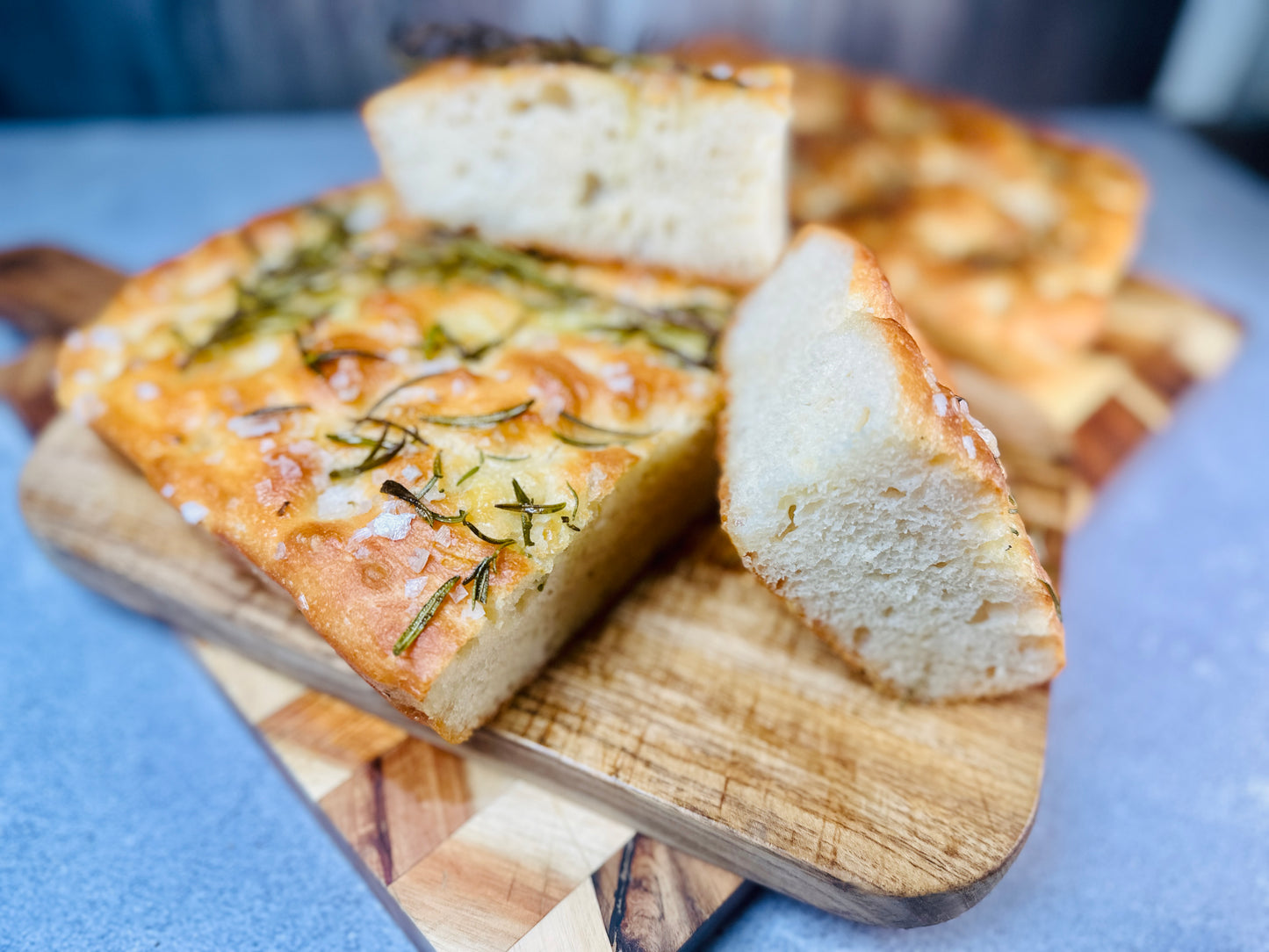 Slices of golden-brown focaccia bread topped with fresh rosemary and flaky sea salt on a wooden cutting board.